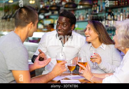 Gruppo di amici maschili e femminili che chiacchierano e bevono birra. Messa a fuoco principale al centro Foto Stock