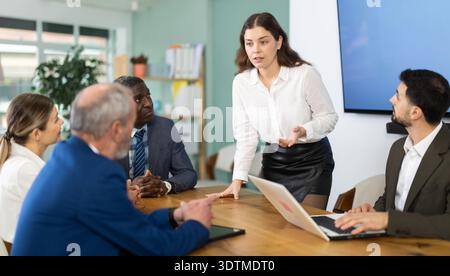 Donna che parla con colleghi seduti a un tavolo Foto Stock