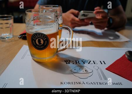 PRAGA, REPUBBLICA CECA - 12 AGOSTO 2024: Un bicchiere di birra ceca siede su un tavolo in un ristorante coreano a Praga. La scena riflette la fusione di Cze Foto Stock