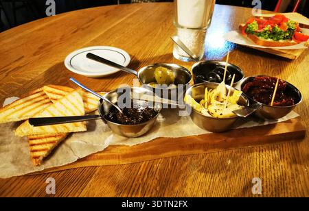 Pane tostato e salse assortite servite in piccole ciotole di metallo su una tavola di legno. Questa immagine rappresenta aperitivi condivisi e momenti informali. Foto Stock
