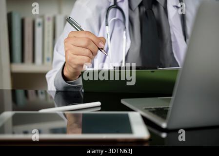 Area di lavoro del medico con appunti di scrittura del medico. Gestione delle cartelle cliniche dei pazienti con stetoscopio, laptop, tablet. Tecnologia sanitaria, elettronica Foto Stock