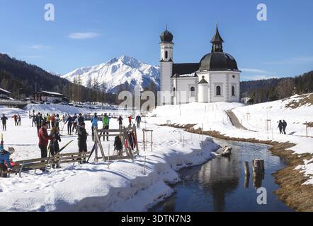 Seefeld, Tirol, Austria - 8 marzo 2020: Sci di fondo su una pista soleggiata lungo un fiume e una chiesa pittoresca Foto Stock