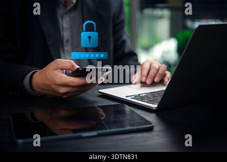Uomo d'affari che utilizza smartphone e laptop con icona di lucchetto digitale, che rappresenta la cybersicurezza, la protezione dei dati, la sicurezza delle password, la privacy online, e se Foto Stock