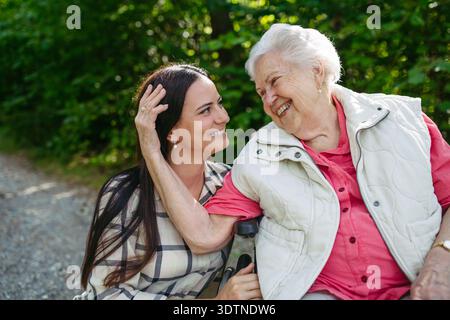 Figlia matura che porta la madre anziana in sedia a rotelle a camminare nella natura. Foto Stock