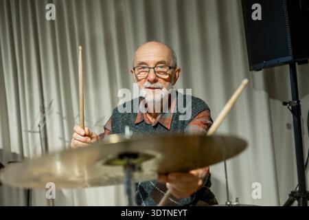 Uomo anziano che si diverte a suonare la batteria. Foto Stock