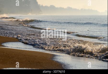Le onde dell'oceano si infrangono su una spiaggia sabbiosa sotto la luce soffusa. Ideale per paesaggi marini, costieri e naturali. Foto Stock