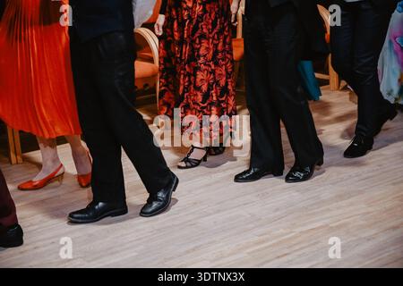 Primo piano di adulti elegantemente vestiti che ballano con scarpe formali durante una festa al chiuso. La vista ritagliata delle gambe e delle calzature mette in risalto il movimento, lo stile, a Foto Stock