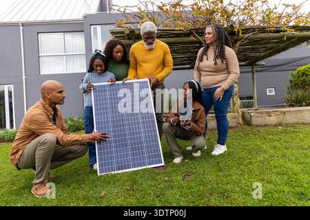 Famiglia afroamericana che esamina un grande pannello solare con un piccolo pannello portatile sul cortile anteriore erboso. Fotovoltaico, array, outdoor, casa, dimostrazione, Foto Stock