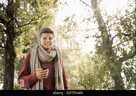 Giovane che ascolta musica nella foresta durante l'autunno Foto Stock