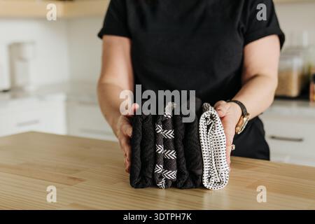 La donna tiene una pila di asciugamani a motivi geometrici sul bancone di fronte a se stessa Foto Stock