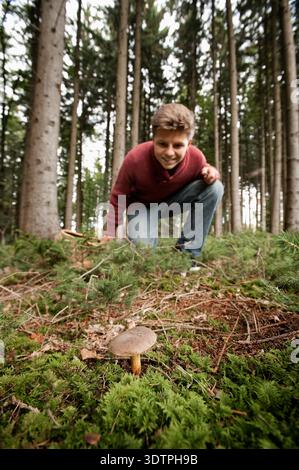 Giovane che accovacciato per raccogliere funghi selvatici nella pineta Foto Stock