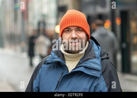 uomo di 35 anni che cammina lungo una strada della città in inverno con abiti caldi Foto Stock