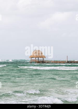 Tradizionale capanna di palapa dal tetto di paglia su un molo di legno sulle acque turchesi di Holbox, Messico. Foto Stock
