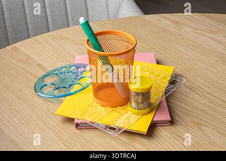 Un vivace allestimento per lo studio con cancelleria colorata, un portapenne in mesh e un blocco note giallo su un tavolo in legno. Foto Stock