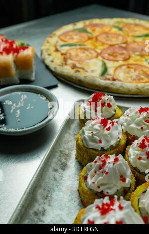 Una deliziosa fusione di sapori: Pizza, sushi e dolcetti in un'esposizione culinaria di diversi piatti su una superficie metallica Foto Stock
