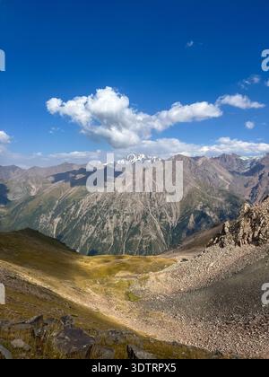 Paesaggio montano mozzafiato con lussureggianti valli verdi e cime innevate sotto un cielo blu brillante Foto Stock