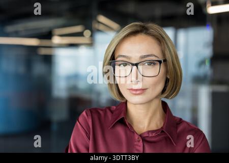 Donna d'affari sicura che indossa eleganti occhiali da vista e una camicia marrone, che ritrae professionalità e leadership mentre guarda la fotocamera in un cont Foto Stock