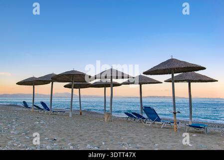 Ombrellone e lettini in spiaggia al tramonto nel Peloponneso in Grecia Foto Stock