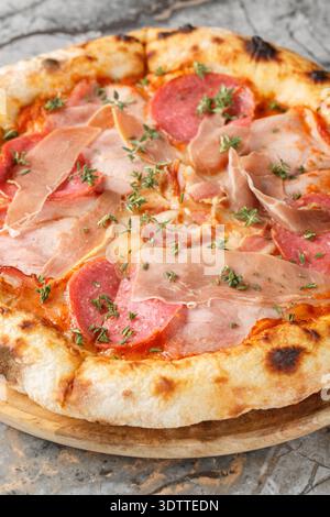 pizza napoletana di carne con prosciutto salame erbe aromatiche primo piano su una tavola di legno sul tavolo. Verticale Foto Stock