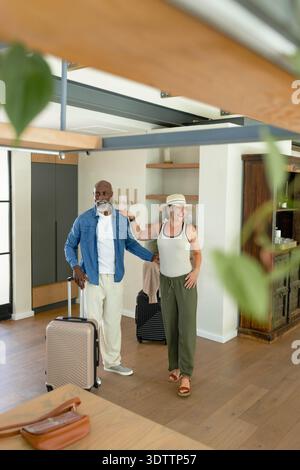 Coppia in piedi in casa con un anziano che tiene la valigia beige mentre la donna tocca la spalla Foto Stock