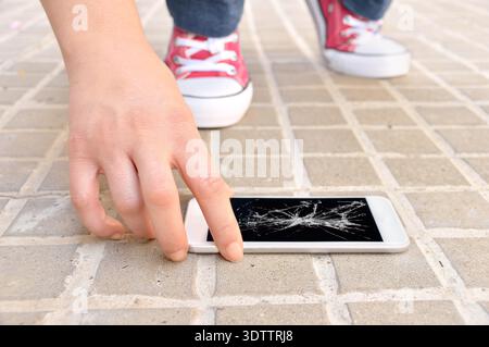 Persona che sceglie uno smartphone rotto con uno schermo del terreno incrinato Foto Stock