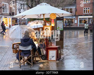 Ritrattista caricatura che disegna un paio sotto ombrelli in un giorno di pioggia a King’s Square, York, North Yorkshire, Inghilterra. Foto Stock