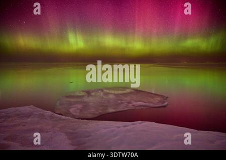 Un'incredibile immagine dell'aurora boreale che mostra vivaci sfumature di verde e rosa nel cielo notturno, riflettendo drammaticamente sulla parte di ghiaccio Foto Stock