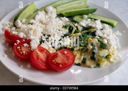 Una deliziosa e nutriente colazione fatta in casa servita su un piatto bianco con omelette di spinaci verdi condite con feta sbriciolata, accompagnata da un piatto Foto Stock