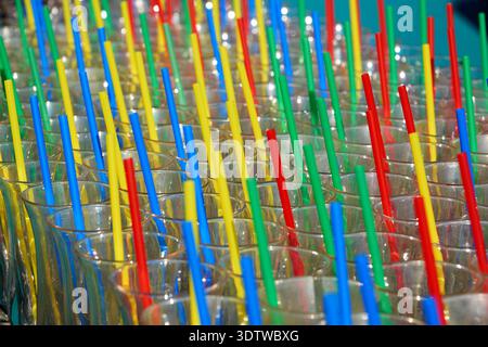 Un primo piano vibrante e dettagliato che cattura numerosi bicchieri da bere trasparenti, ciascuno dotato di una cannuccia di plastica dai colori vivaci. Le cannucce sono pr Foto Stock