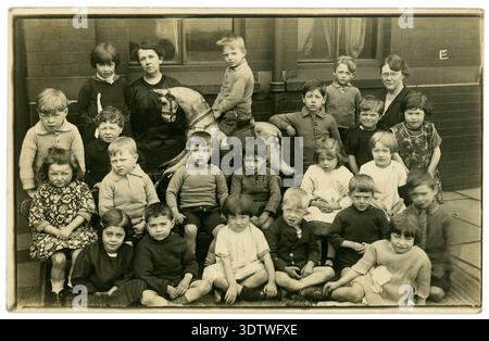 Gruppo ritratto anni '1900 bambini della scuola infantile in strada fuori dalla scuola elementare urbana anni '1900, cavallo a dondolo, forse quartiere povero circa 1925 Regno Unito Foto Stock