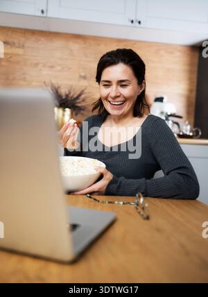 Laughing Girl che guarda Un video su Un laptop e mangia Popcorn Foto Stock