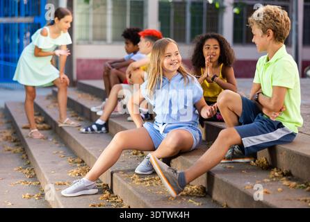 Amici dei tweenager felici seduti sui gradini all'aperto e chiacchierando Foto Stock
