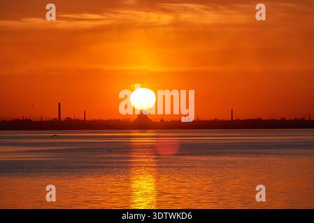 Un'ampia ripresa mozzafiato che cattura un tramonto rosso e arancione acceso o un'alba su un corpo d'acqua, probabilmente il Golfo di Finlandia. Il grande, bril Foto Stock
