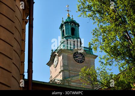 Una vista dall'angolo basso verso l'alto cattura la storica torre dell'orologio di Storkyrkan (cattedrale di Stoccolma) contro un vivace cielo blu. Caratteristiche della torre Foto Stock