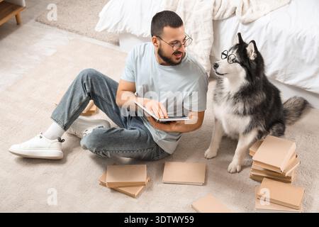 Bel giovane e simpatico cane da husky con gli occhiali che leggono libri sul pavimento a casa Foto Stock