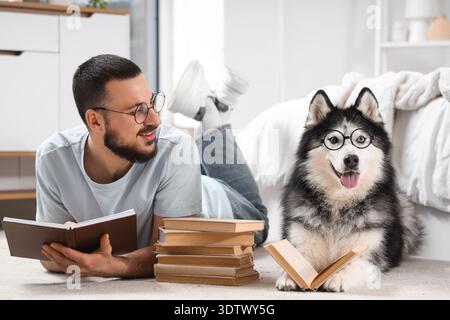 Bel giovane e simpatico cane da husky con gli occhiali che leggono libri sul pavimento a casa Foto Stock