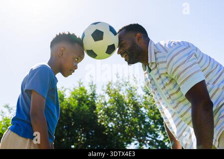 Uomo maturo che indossa una camicia a righe, ragazzo giovane che indossa una T-shirt blu che preme la palla da calcio nel cortile posteriore Foto Stock