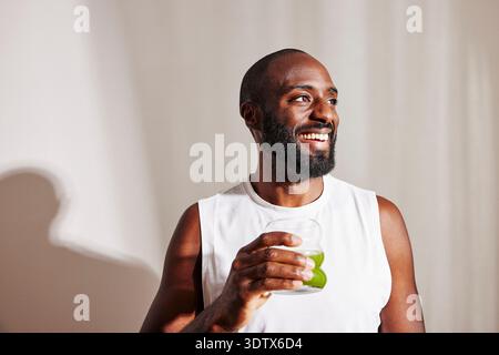 Uomo sorridente con barba che guarda lontano tenendo in mano il bicchiere per succo di disintossicazione Foto Stock