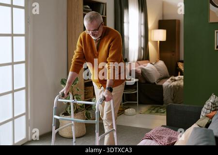 Uomo caucasico anziano che usa Walker mentre si trova in un soggiorno moderno Foto Stock