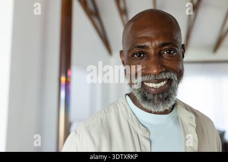 Senior afroamericano sorridente, con camicia beige e tee blu a casa con specchio Foto Stock