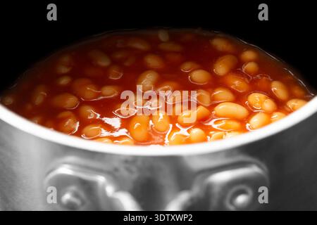 Fagioli in scatola, in salsa di pomodoro, cotti su sfondo di una pentola in acciaio inossidabile Foto Stock