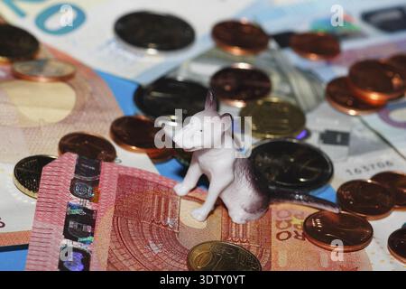Figura in miniatura di Bull terrier seduta su monete in euro circondate da banconote su sfondo blu, Renania settentrionale-Vestfalia, Germania Foto Stock