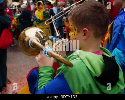 Langenthal, Berna, Svizzera. 21 febbraio 2026. Carnevale di Fasnacht in città. Il ragazzo in costume verde gioca a trombone in una sfilata con costume colorato Foto Stock