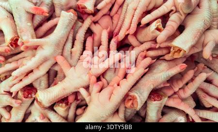 Vista ravvicinata ad angolo alto di un grande mucchio di piedi di pollo crudi con pelle rosa e artigli testurizzati, preparati per la vendita in un mercato alimentare locale. Foto Stock