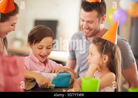 Ragazzo, famiglia e festa con regalo di compleanno a casa per desiderio, benedizione o legame. Mamma, papà e bambino eccitato che apre il regalo con il sorriso Foto Stock