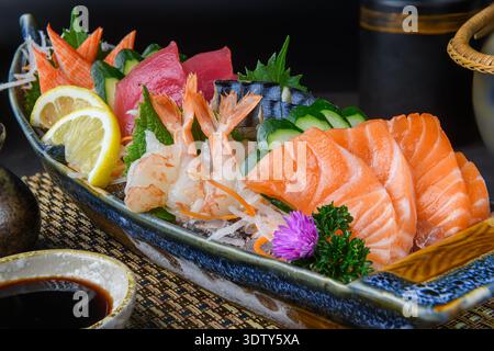 Un piatto di sashimi assortito di prima qualità con gamberi dolci, tonno, salmone, bastoncini di granchio, cetrioli, e fette di limone, splendidamente organizzate per un gourmet Foto Stock