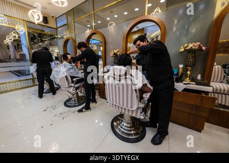 I barbieri in uniforme nera tendono ai clienti in un moderno salone di parrucchiere con specchi ad arco all'interno dell'Omaxe Mall a Chandni Chowk nella vecchia Delhi. Foto Stock
