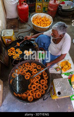 Un venditore ambulante di patatine fritte di arancia in grandi tini di metallo in una tradizionale bancarella di cibo a Chandni Chowk nel quartiere della vecchia Delhi. Foto Stock