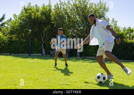 Padre e figlio afroamericani che giocano a calcio sul prato del giardino, dribbling di palle in bianco e nero Foto Stock