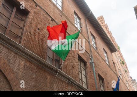 07.06.25, Siena, Italia, primo piano della bandiera italiana sventolando sulla facciata dell'edificio storico. Simbolo nazionale e identità culturale dell'Italia Foto Stock